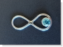 zu sehen ist ein Kettenanhänger in Silber 935 in der Form eines hängenden Endloszeichens. In der unteren Schleife ist ein Zirkon in Aquamarinfarbe eingearbeitet